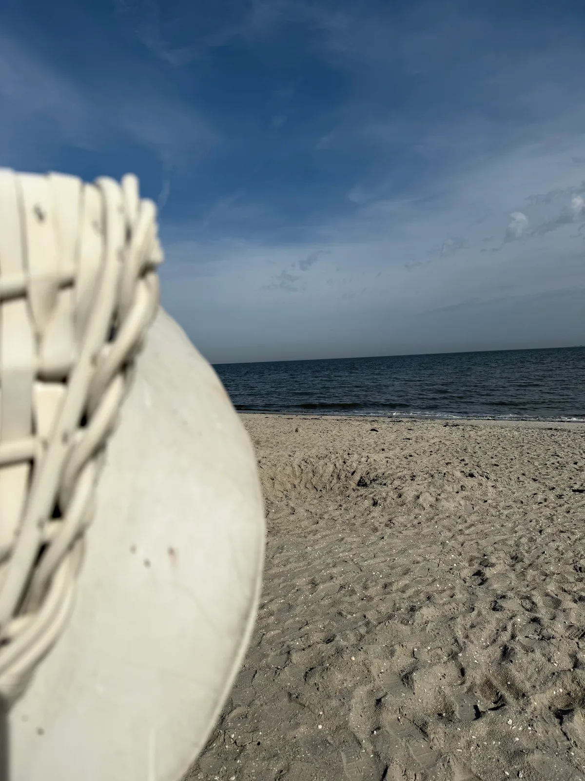 Die Rundung eines weißen Strandkorbs ragt ins Bild, dahinter der leere Strand und die Nordsee.